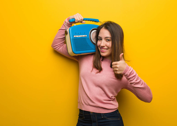 Nuori söpö nainen tilalla vintage radio hymyilee ja nostaa peukalo ylös
 - Valokuva, kuva