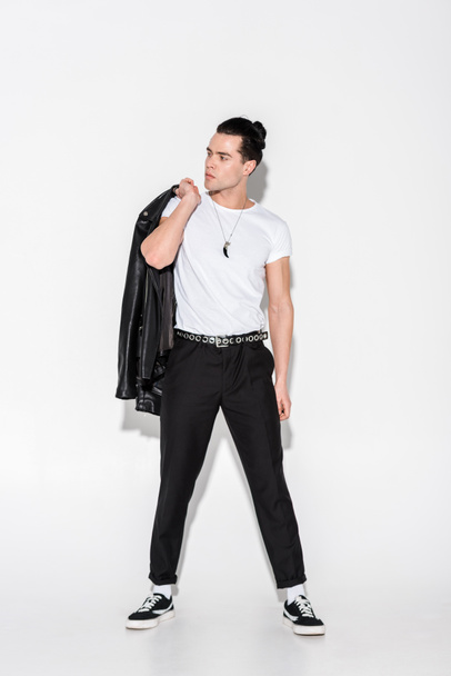 handsome man in white t-shirt holding leather jacket while standing on white  - Fotografie, Obrázek