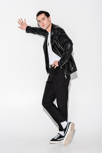 handsome man in black leather jacket standing with crossed legs on white  - 写真・画像