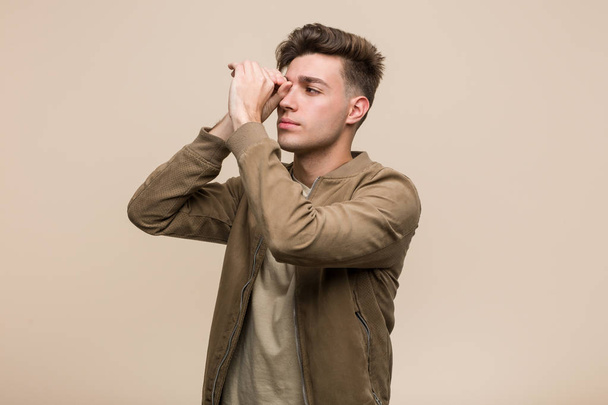 Young caucasian man wearing a brown jacket looking far away keeping him hand on forehead. - Photo, Image