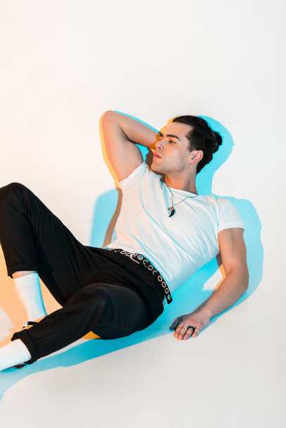 handsome man in white t-shirt lying on white with illumination  - Photo, image