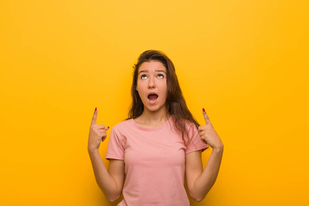 Genç Avrupalı kadın sarı arka plan üzerinde izole boş bir boşluk gösteren kadar her iki ön parmak ile gösterir. - Fotoğraf, Görsel