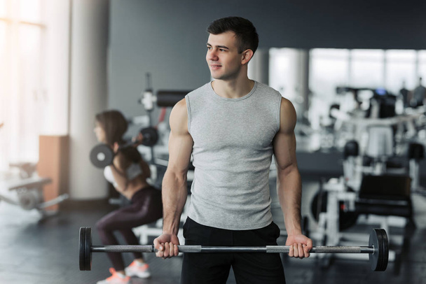 Красивый мускулистый мужчина тренируется с гантелями в спортзале
. - Фото, изображение