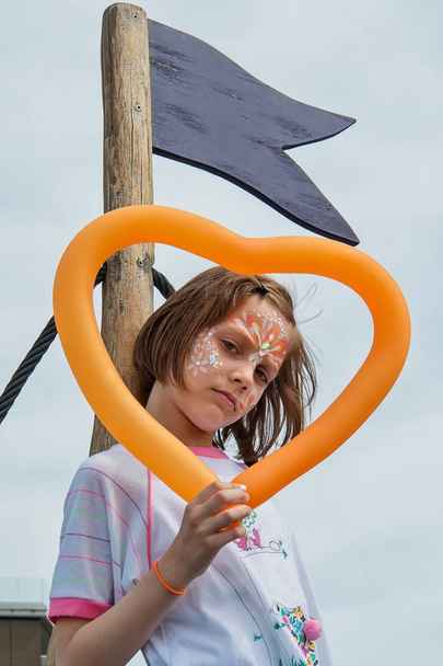 A pretty girl has a face painting and holding a balloon in shape heart - Photo, Image