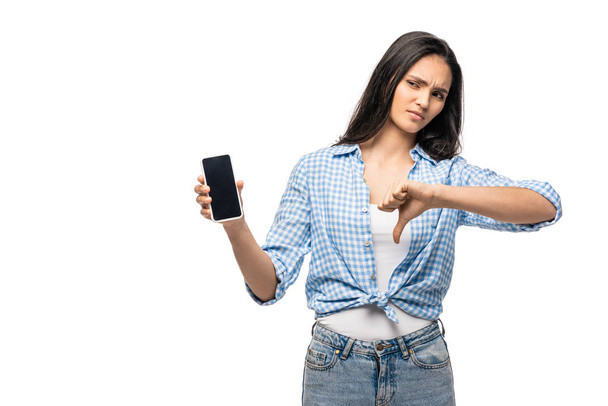 chica decepcionada sosteniendo teléfono inteligente con pantalla en blanco y mostrando el pulgar hacia abajo aislado en blanco
 - Foto, imagen