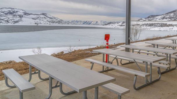 Panorama Eating area inside a pavilion overlooking a lake amid the snowy landscape - Photo, Image
