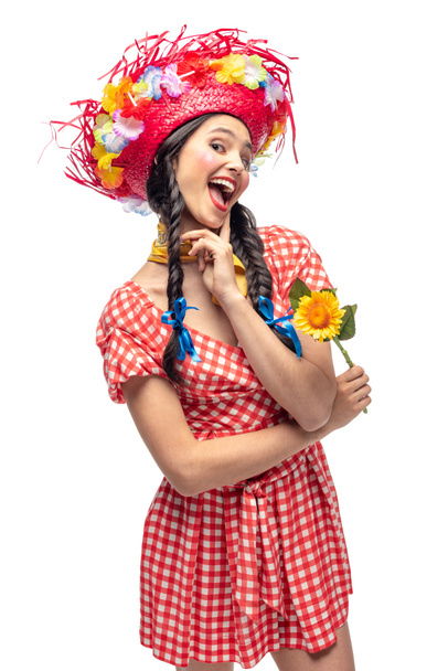 menina animado em roupas festivas e chapéu de palha tocando queixo isolado no branco
 - Foto, Imagem