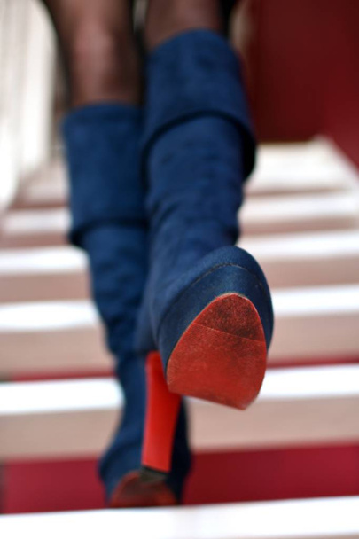 Jambes féminines en bottes à talons hauts bleus avec semelles rouges descendent les escaliers blancs, vue de face
  - Photo, image