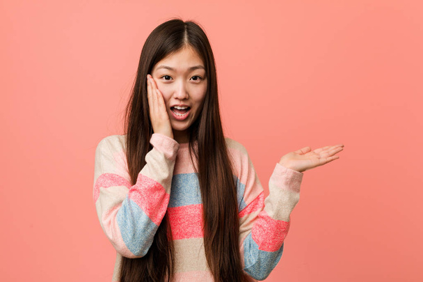La giovane donna cinese fresca tiene lo spazio di copia su una palma, tenga la mano sopra guancia. Stupito e felice
. - Foto, immagini