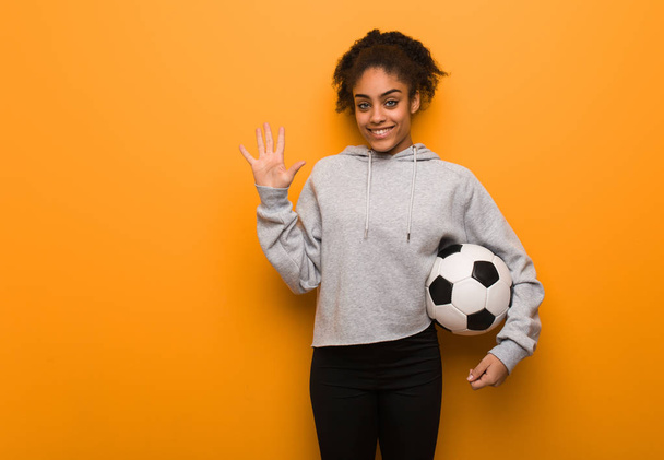 Молодая черная женщина показывает номер пять. Холдинг футбольный мяч
. - Фото, изображение