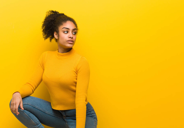 Young black woman sitting over an orange wall - Foto, afbeelding
