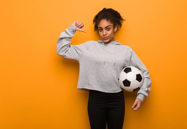 Молодая фитнес черная женщина указывает пальцем, пример для подражания. Холдинг футбольный мяч
. - Фото, изображение