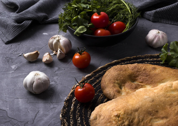 Tasty fresh tandoori bread on gray table with tomato, garlic and parsley. National georgian cuisine and food.  - 写真・画像