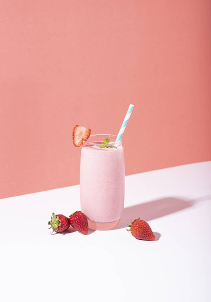Strawberry smoothie in glass with straw and scattered berries  - Фото, зображення