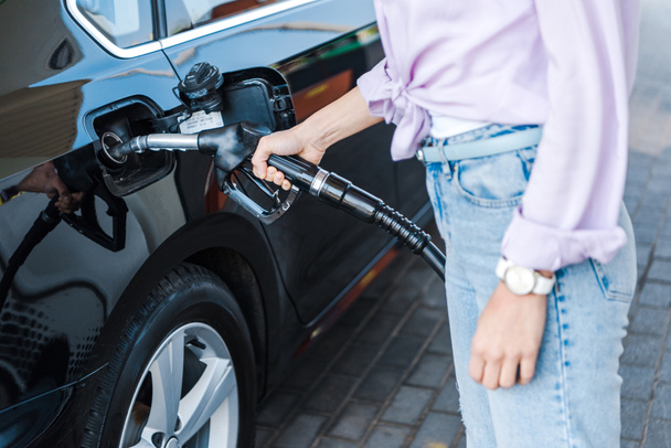 oříznutý pohled ženy držící palivovou pumpu při tankování černého auta s benzinem  - Fotografie, Obrázek