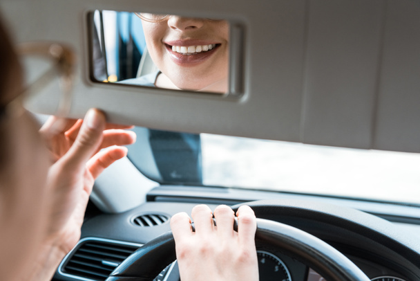 車の中で鏡を見ている笑顔の女性のトリミングされたビュー  - 写真・画像