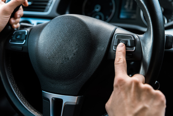 cropped view of man pointing with finger at button while holding steering wheel - 写真・画像