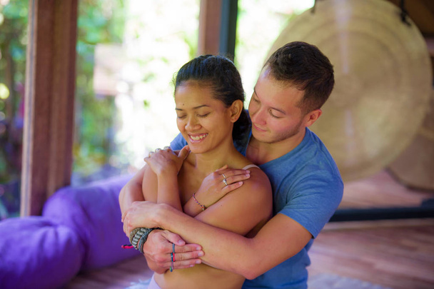 young beautiful and exotic Asian Balinese woman receiving body healing Thai massage by attractive Caucasian masseur man at traditional wellness spa garden  - Photo, Image