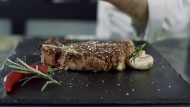 Chef peppering grilled meat at cut board. Man hands pepper steak in slow motion - Πλάνα, βίντεο