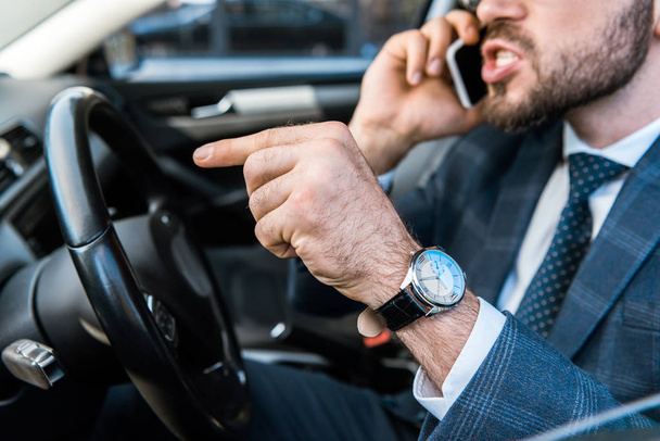 selective focus of angry bearded businessman talking on smartphone and pointing with finger  in car  - Foto, Imagem
