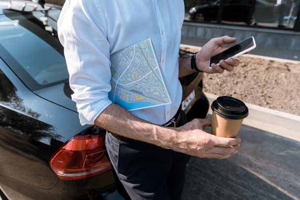 vista cortada do homem usando smartphone enquanto segurando copo de papel perto do carro
  - Foto, Imagem