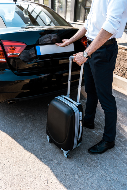vue recadrée de l'homme d'affaires ouvrant le coffre de la voiture tout en étant debout avec des bagages
 - Photo, image
