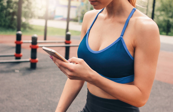 Фотография привлекательной девушки в спортивной одежде, занимающейся тренировками с мобильным устройством на улице. Здоровый образ жизни в городе
 - Фото, изображение