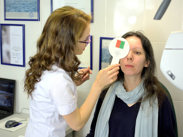 νεαρή όμορφη γυναίκα υποβλήθηκε σε εξέταση οπτικής οξύτητας με οφθαλμίατρο οφθαλμίατρο οπτικό, χαμηλό βάθος πεδίου - Φωτογραφία, εικόνα