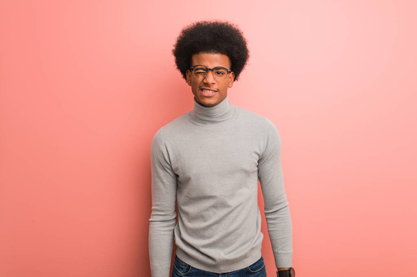 Fiatal afro-amerikai férfi egy rózsaszín fal kacsintás, vicces, barátságos és gondtalan gesztus - Fotó, kép