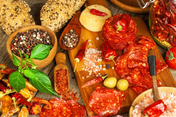 sausage or salami with chili pepper with herbs on wooden table. Spicy salami with chili. Unhealthy Fat Food. - Photo, image