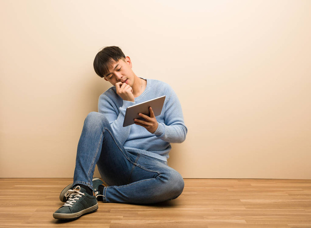 Młody Chińczyk siedzący za pomocą tabletu zrelaksowany myśląc o czymś patrząc na przestrzeń kopii - Zdjęcie, obraz
