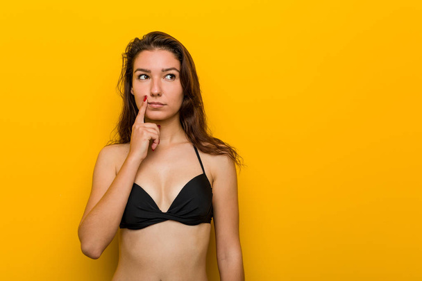 Молодая европейская женщина в бикини смотрит в сторону с сомнительным и скептическим выражением
. - Фото, изображение