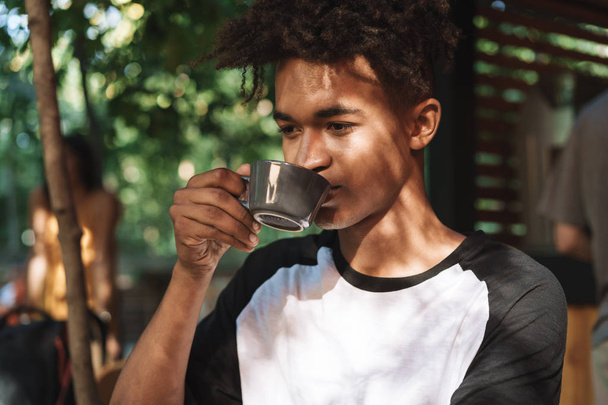 Smiling african young man drinking coffee at the cafe - 写真・画像