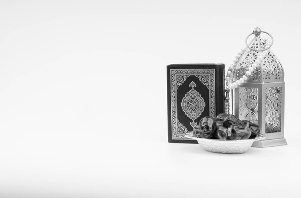 Lantaarn, dadels, Koran en rozenkrans op witte achtergrond met selectieve focus en gewas fragment. Ramadan, religie en copy Space concept. Zwart-wit concept - Foto, afbeelding