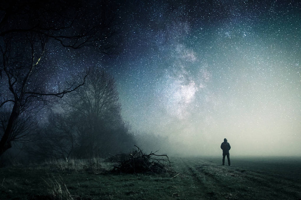 Een eenzame Hooded figuur staan op een pad op een spookachtige Misty Night. - Foto, afbeelding