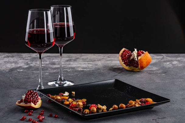 twee glazen rode wijn met granaatappel fruit en noten. donkere achtergrond. - Foto, afbeelding