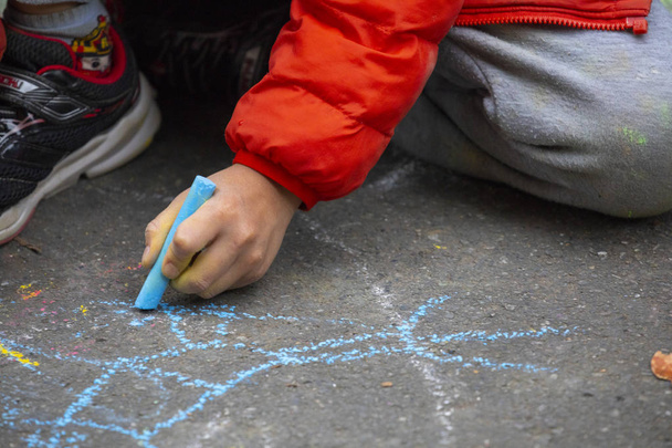 Child on the outdoor park floor, drawing doodles with chalk happy - Photo, Image