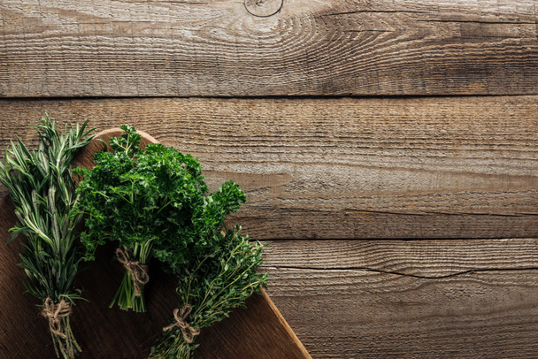 top view of green rosemary, parsley and thyme on chopping board on wooden weathered table with copy space - Fotoğraf, Görsel