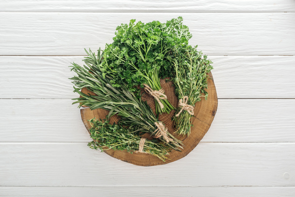 top view of green parsley, rosemary and thyme on brown stump on white wooden table - Photo, Image