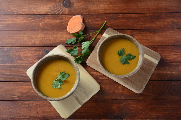 Сладкий картофельный и морковный суп со сметаной в деревянной миске. Апельсиновый овощной суп. Веганская еда
 - Фото, изображение