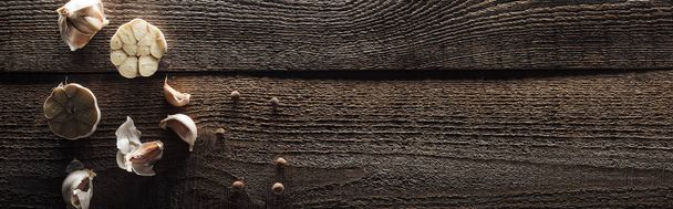 panoramic shot of garlic cloves and black pepper on wooden table - Photo, Image