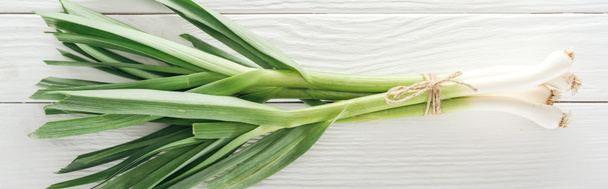 top view of fresh green leek on white wooden table, panoramic shot - Foto, afbeelding