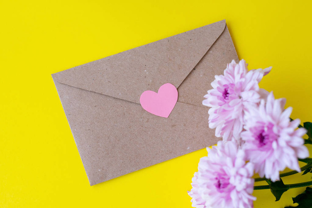 Love envelope with pink chrysanthemum flowers with pink heart on bright yellow bacground - Foto, Imagen