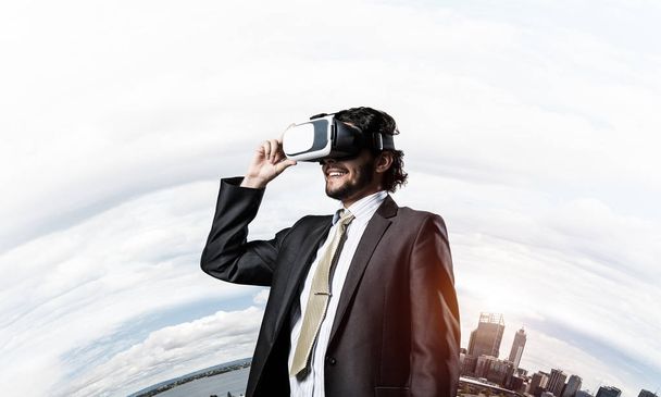 Young handsome businessman in virtual helmet against cityscape background - Fotoğraf, Görsel