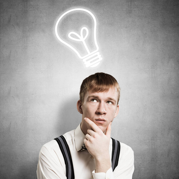 Redhead student thinking about some problem. Clever boy on background of grey wall with idea lightbulb sketch drawing overhead. Young businessman wears shirt and suspenders. New idea generation. - Foto, Imagem