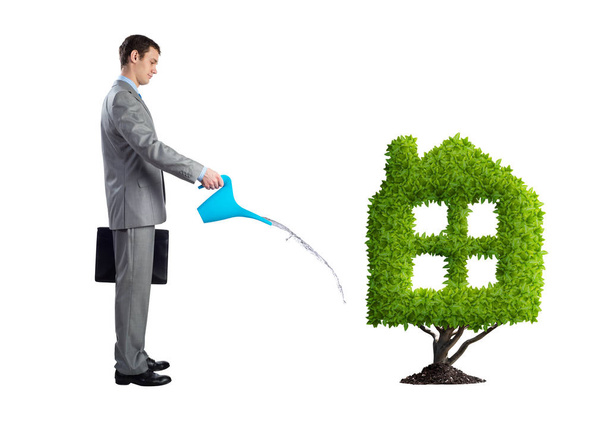 Businessman watering green plant in shape of house isolated on white background. Green and eco friendly technology. Business development to success. Real estate company growth. - Photo, Image