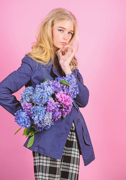 Fashionable coat. Must have concept. Clothes and accessory. Woman blonde hair posing coat with flowers bouquet. Girl fashion model wear coat for spring and autumn season. Trench coat fashion trend - Fotó, kép