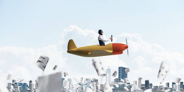 Business accounting and statistics concept with funny pilot. Aviator driving propeller plane above falling paper sheets with infographics. Young man flying in small airplane above paperwork. - Photo, Image