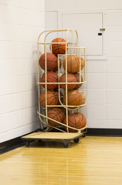 Пачка баскетбольных мячей в держателе для проволоки в углу спортзала
 - Фото, изображение