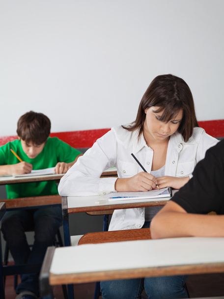 Школа девушка пишет бумаги на рабочем столе во время экзамена
 - Фото, изображение